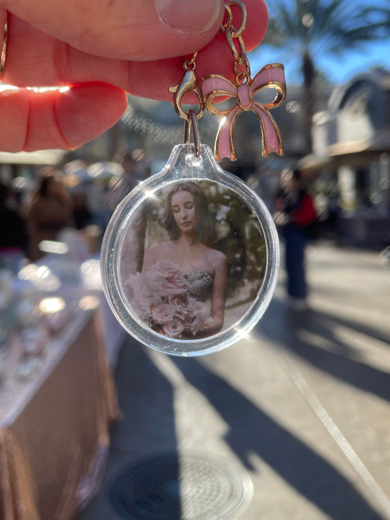 Keychain with a clear pendant featuring a photo of a woman, held by a hand outdoors. Custom photo keychain
